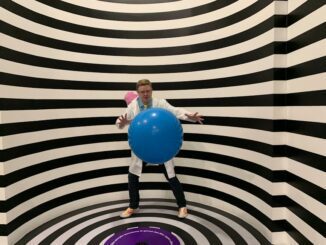 illuseum berlin - A man wearing a lab coat poses with a blue ball in a striped illusion room.
