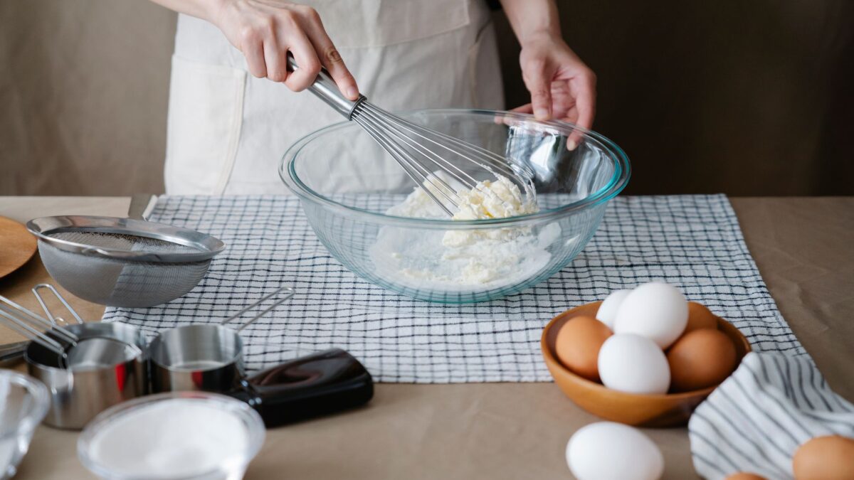 Handmixer auf einer Küchenarbeitsplatte neben Rührschüssel und Laptop