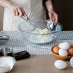 Handmixer auf einer Küchenarbeitsplatte neben Rührschüssel und Laptop