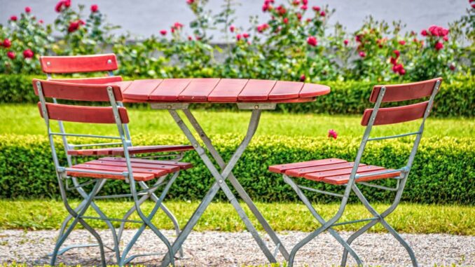 siena garden - Cozy outdoor garden setup with red chairs and table, surrounded by blooming roses.