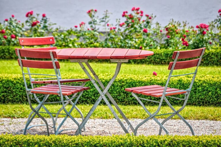 siena garden - Cozy outdoor garden setup with red chairs and table, surrounded by blooming roses.