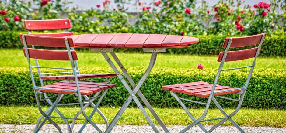 siena garden - Cozy outdoor garden setup with red chairs and table, surrounded by blooming roses.